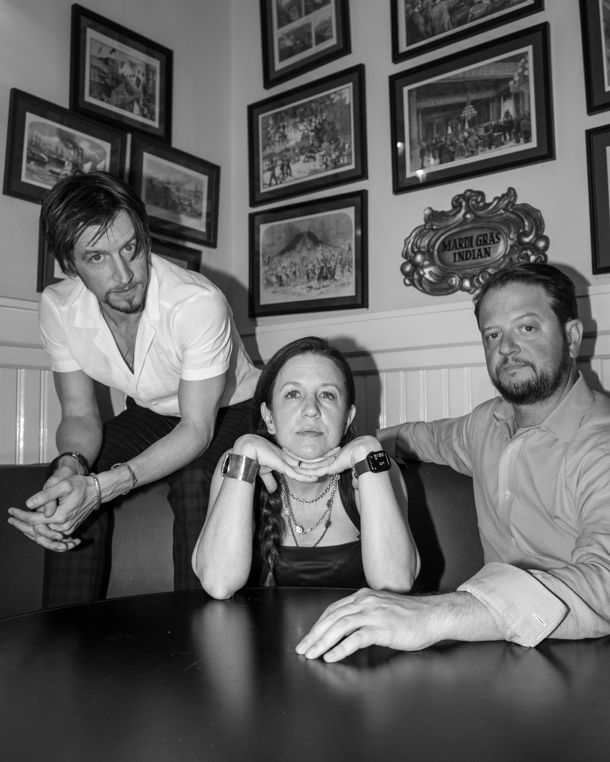 Three people at a table beneath a wall of framed prints
