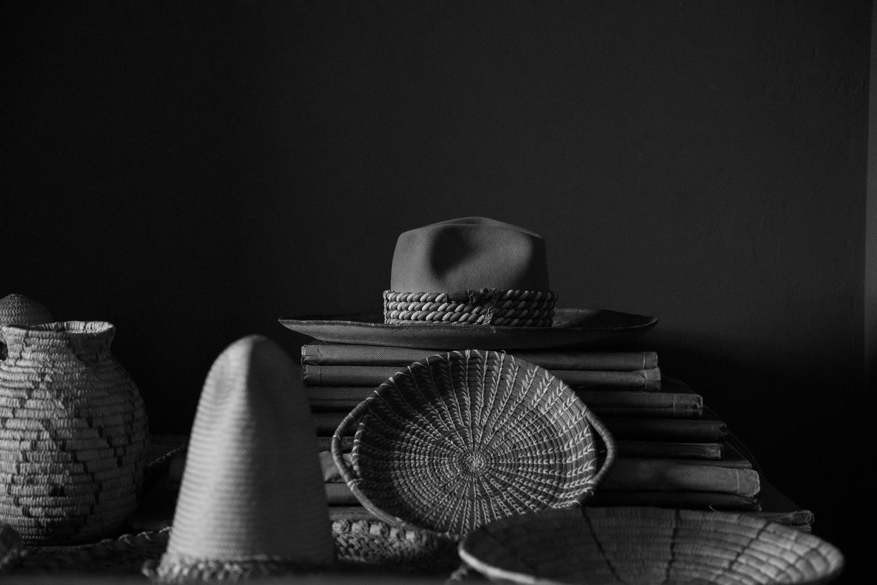 A felt hat resting on a stack of books beside woven Yucatán baskets
